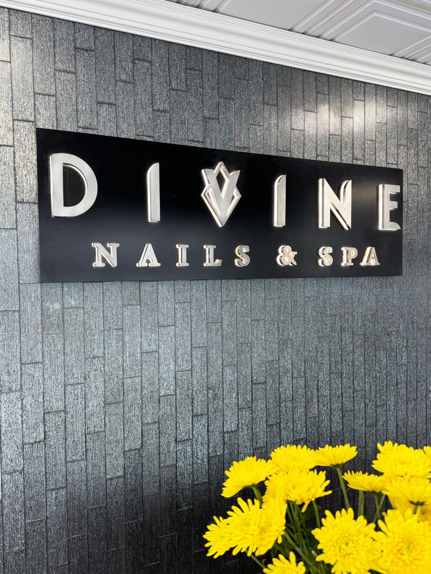 Divine Nails & Spa silver signage on a textured stone wall